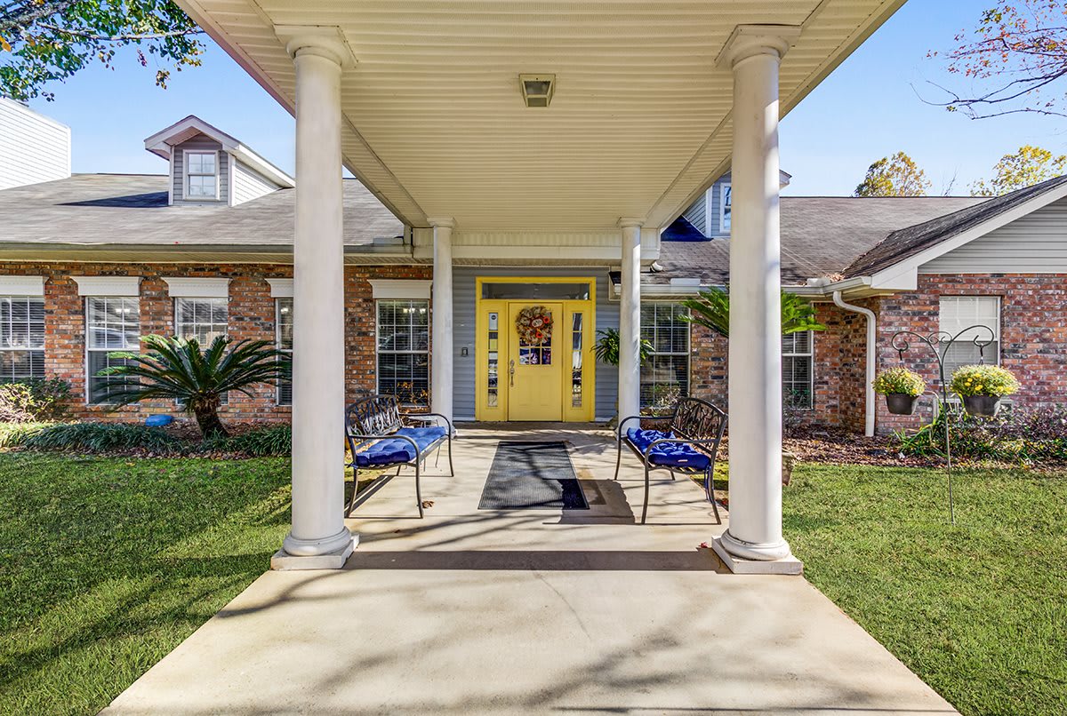 A welcoming entrance to a house featuring a yellow door, flanked by two benches and supported by white columns.