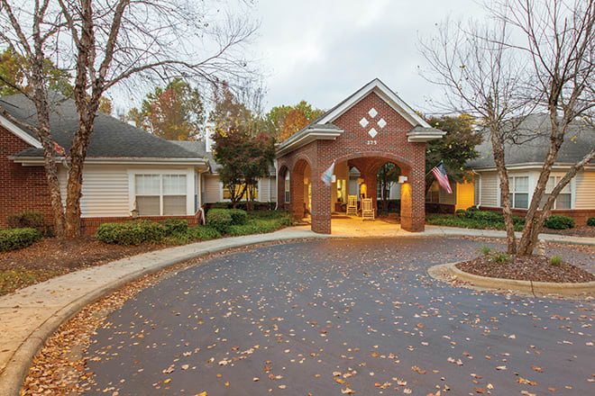 A brick building entrance with a circular driveway surrounded by autumn trees.