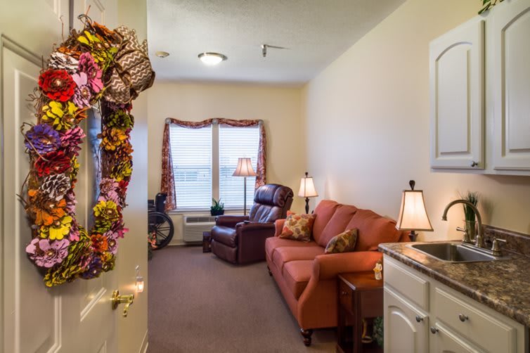 A cozy living room with a sofa, armchair, and decorative wreath on the door.