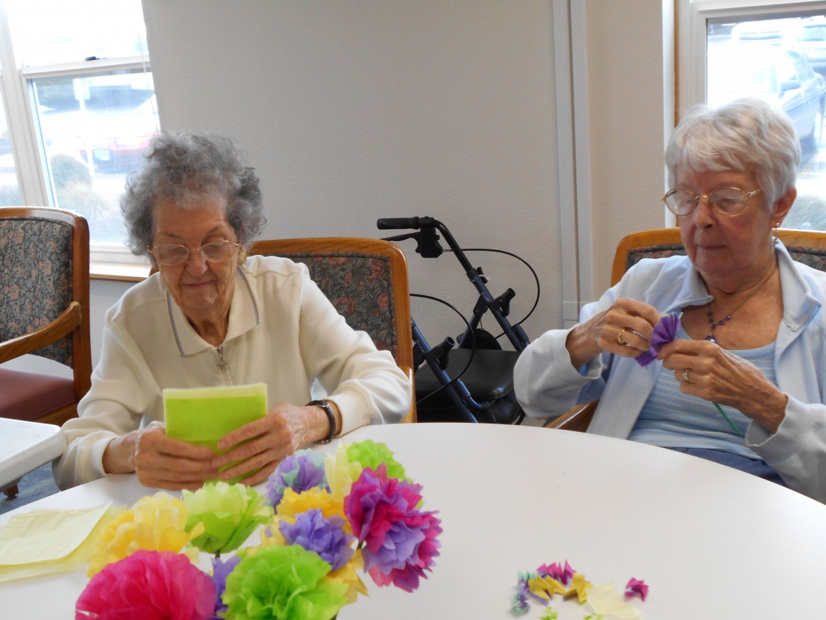 Two elderly individuals engaging in a crafting activity with colorful flowers at a table.