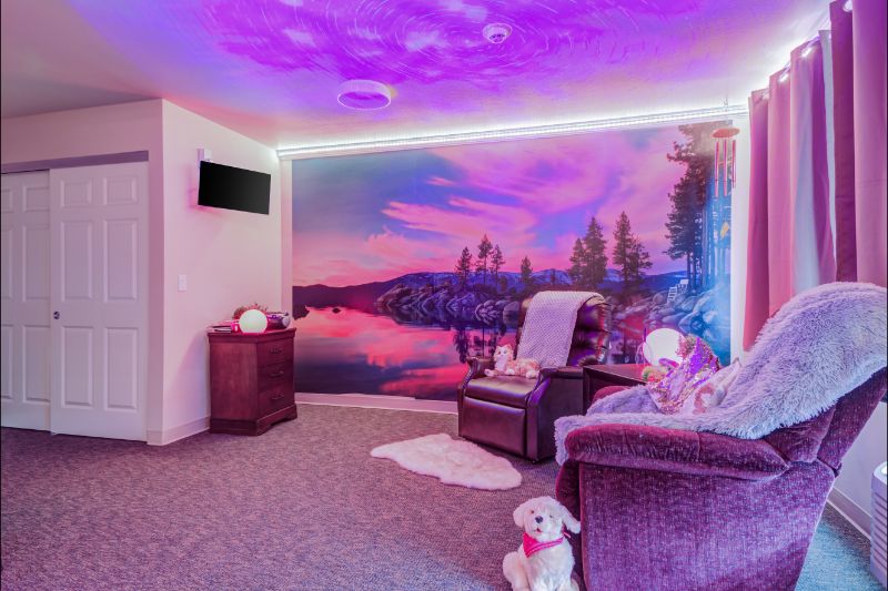 A cozy room featuring plush chairs, purple ambient lighting, and a serene nature scene mural on the wall.