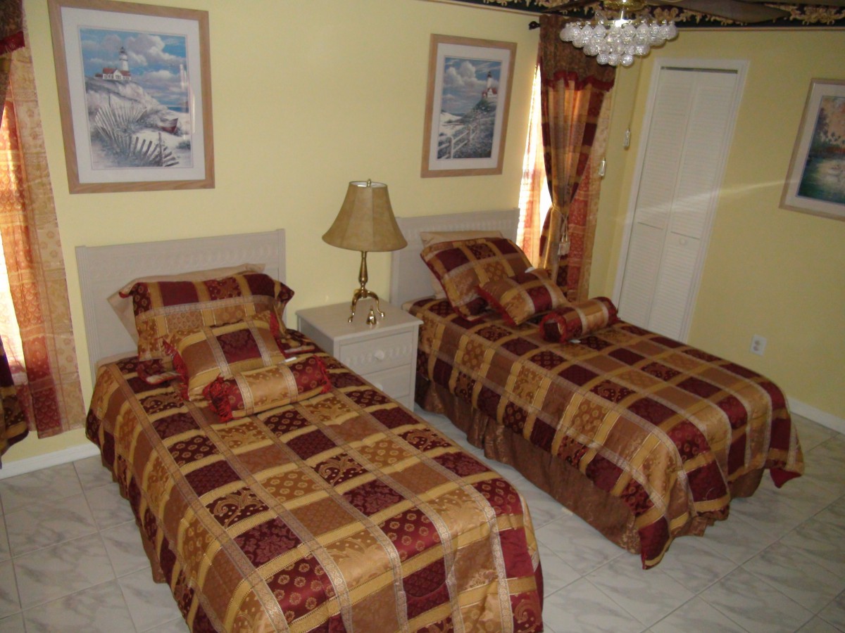 A cozy bedroom with twin beds featuring patterned covers, decorated with framed pictures and a chandelier.