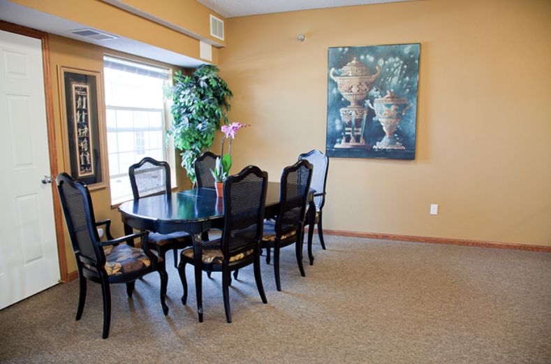 A dining room with a black table and chairs, an artwork on the wall, and a window providing natural light.
