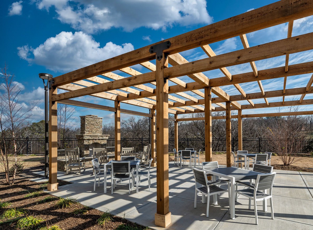 An outdoor seating area under a wooden pergola with tables and chairs on a sunny day.