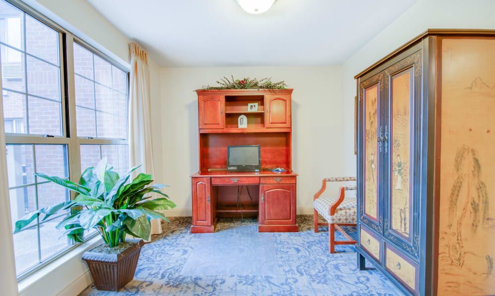 A cozy home office space with a wooden desk and bookshelf, a computer setup, and indoor plants.
