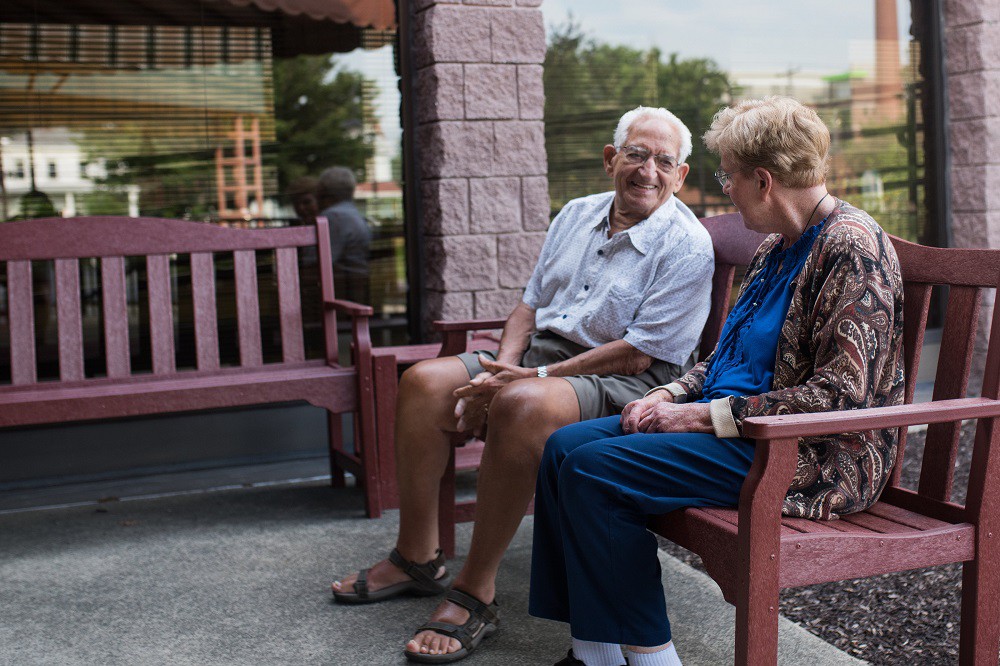 An elderly couple sitting on a bench, engaged in conversation.