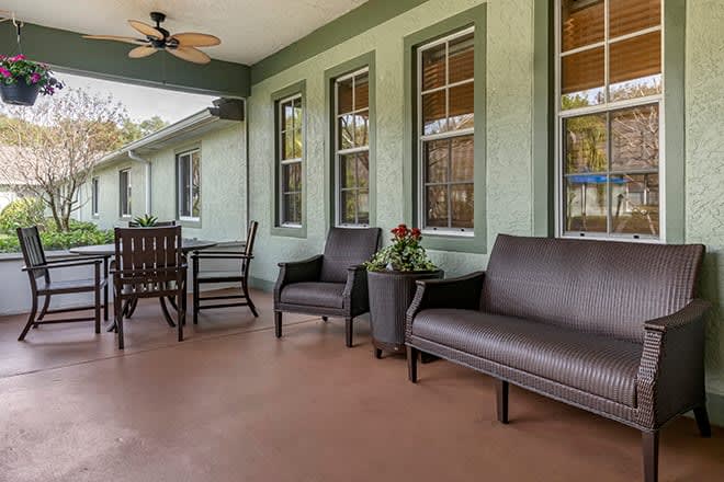 A cozy patio area with comfortable seating and a table, surrounded by green walls and windows.