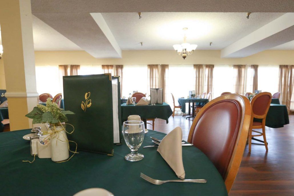 A neatly set dining table in a well-lit restaurant interior, featuring a menu, folded napkin, and glassware.
