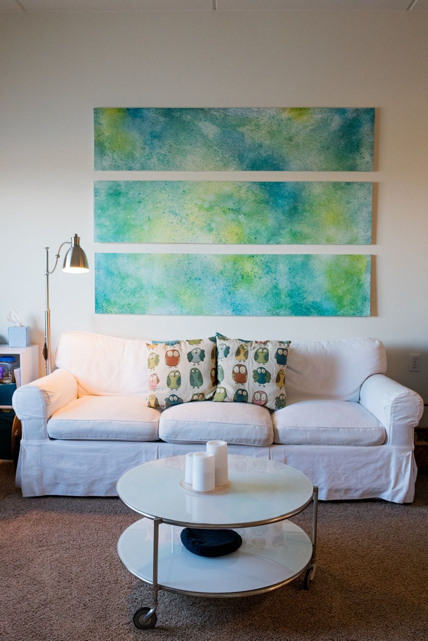 A cozy living room featuring a white sofa with colorful cushions, complemented by abstract artwork on the wall.