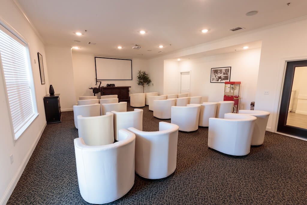 A modern conference room with a projector screen and white armchairs arranged for a presentation.