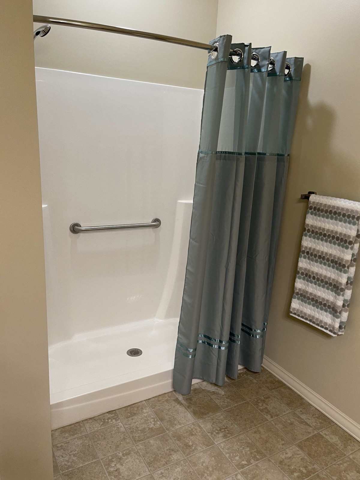 A bathroom with a shower area featuring a blue curtain and a grab bar.