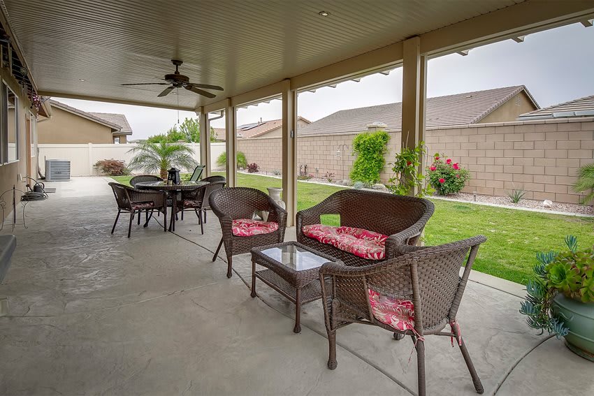 A cozy covered patio with wicker furniture and a view of a neat backyard garden.