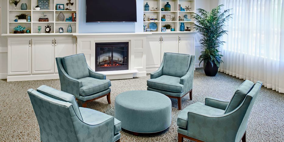 A cozy living room with teal chairs, a round ottoman, and a fireplace surrounded by built-in bookshelves.