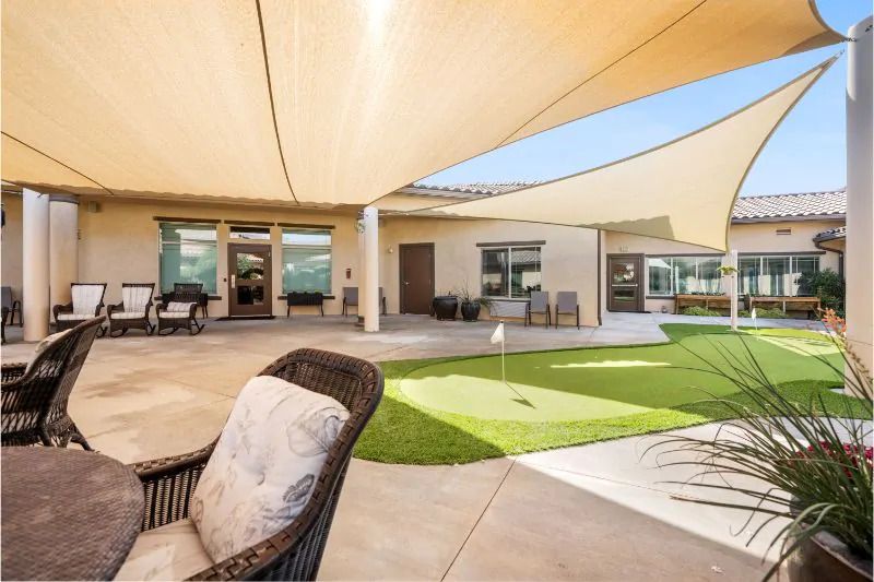 A modern backyard with shade sails, outdoor seating, and a golf putting green on a sunny day.