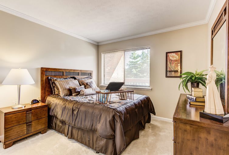 A cozy bedroom featuring a bed with brown bedding, wooden furniture, and large windows with natural light.