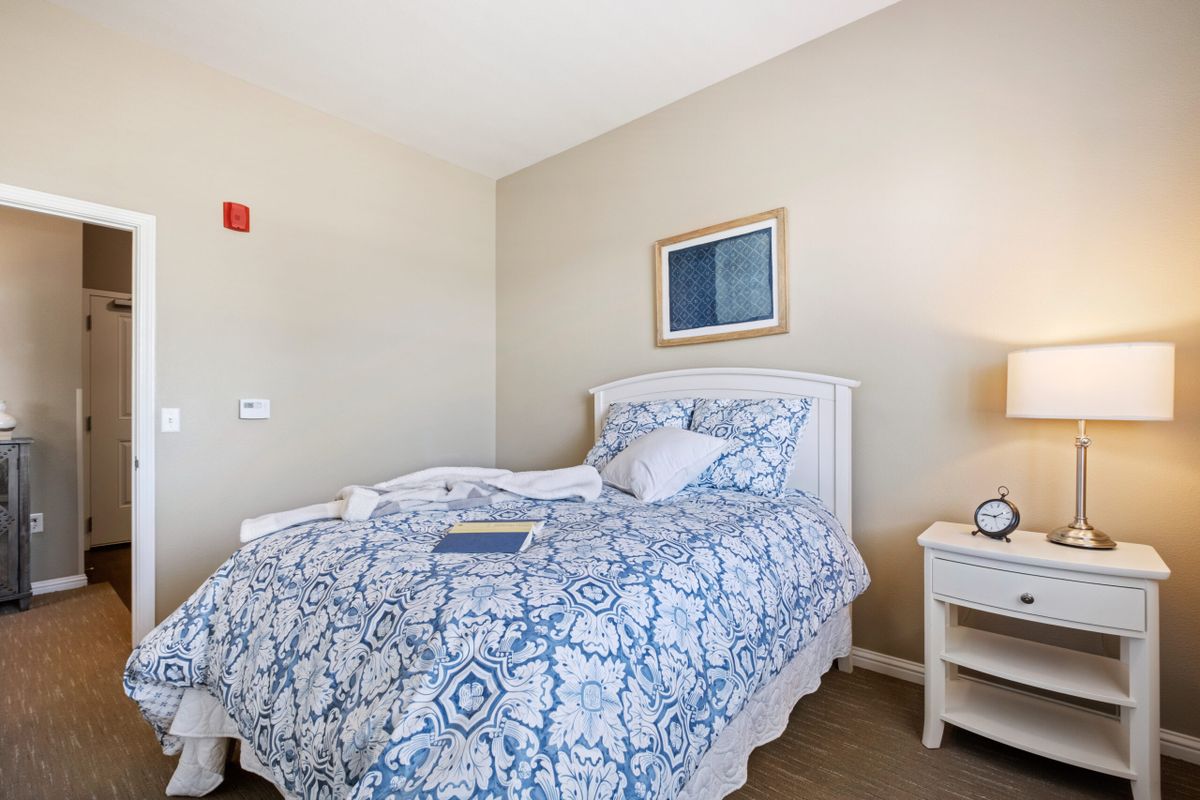 A cozy bedroom with a patterned bedspread and a nightstand with a lamp.