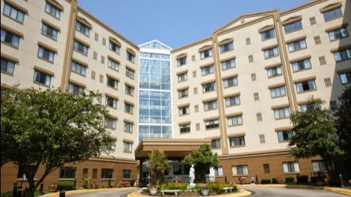 A multi-story hotel building with a central glass atrium and landscaped entrance.