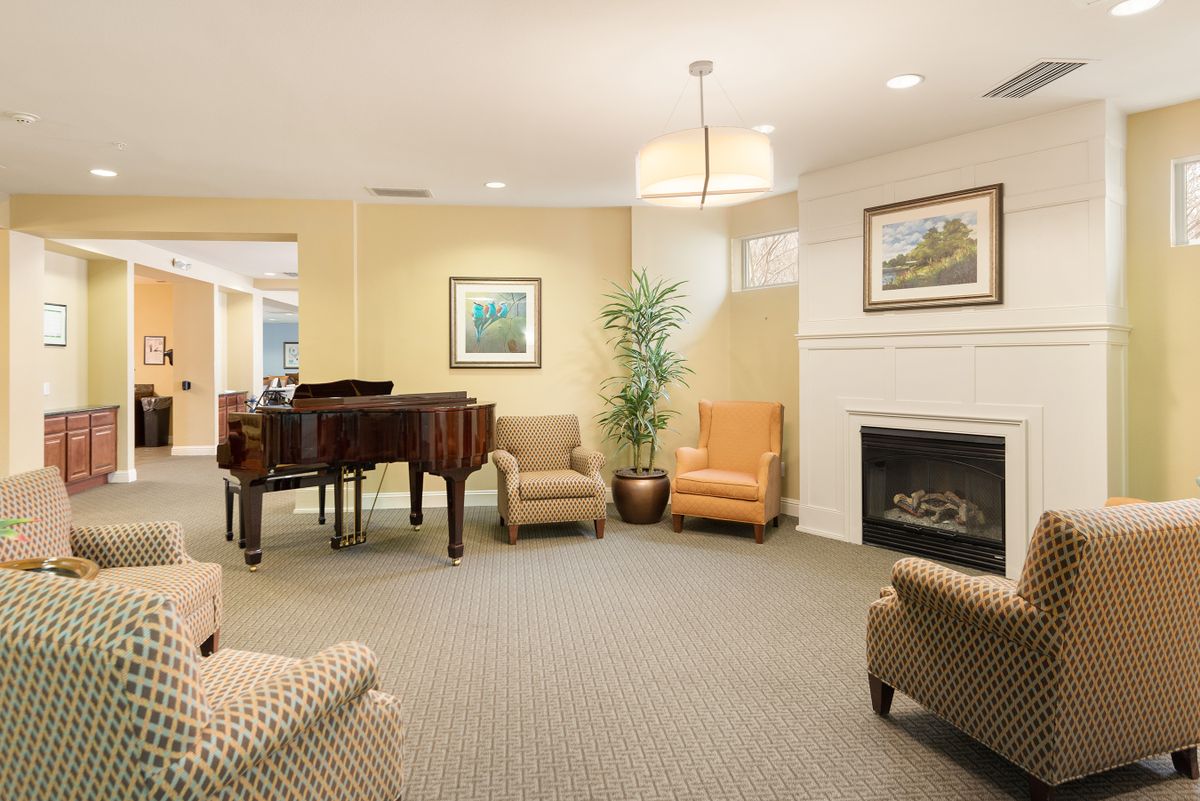 A cozy living room featuring a grand piano, comfortable seating, a fireplace, and artwork on the walls.
