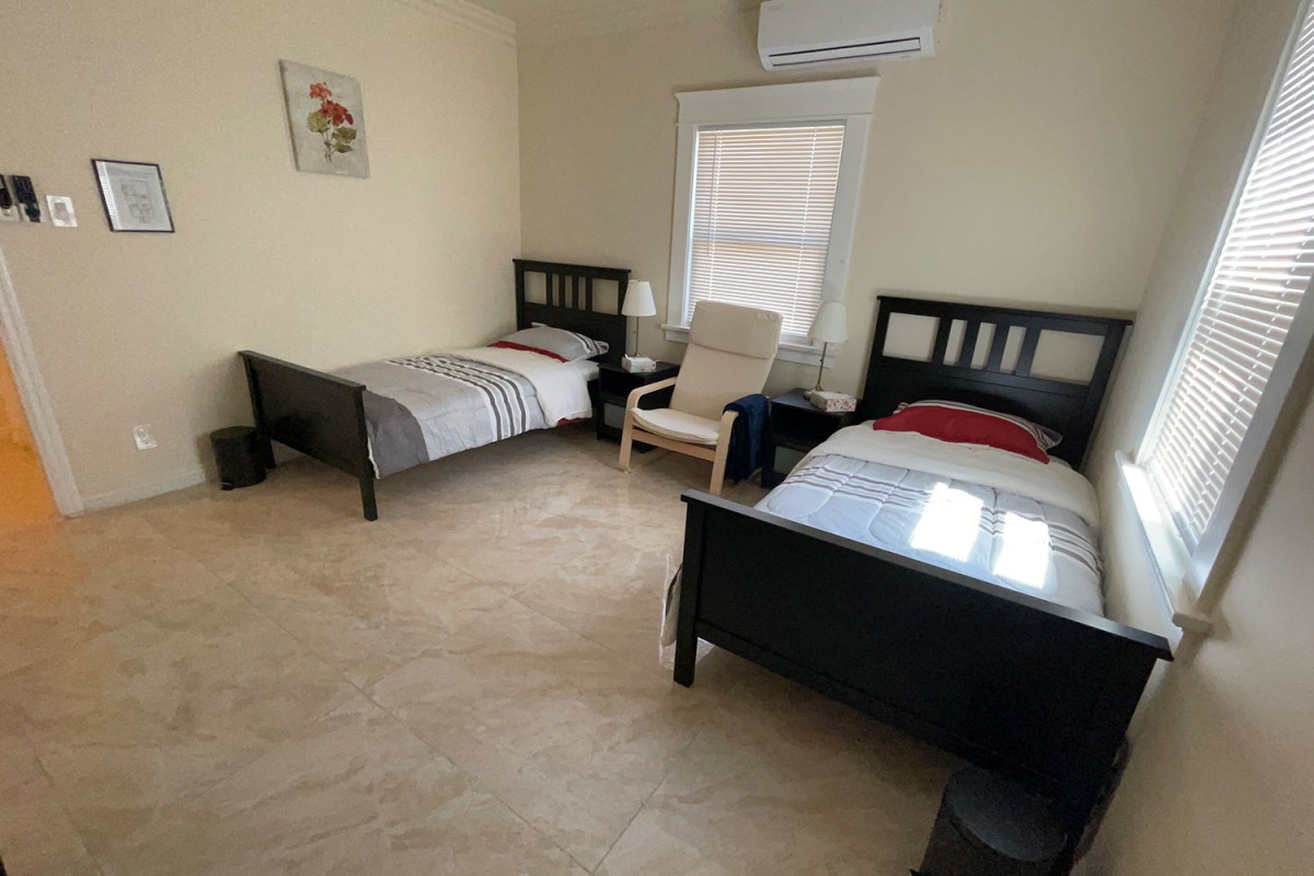 A minimalist bedroom with two twin beds, a chair, and a nightstand beneath a window.