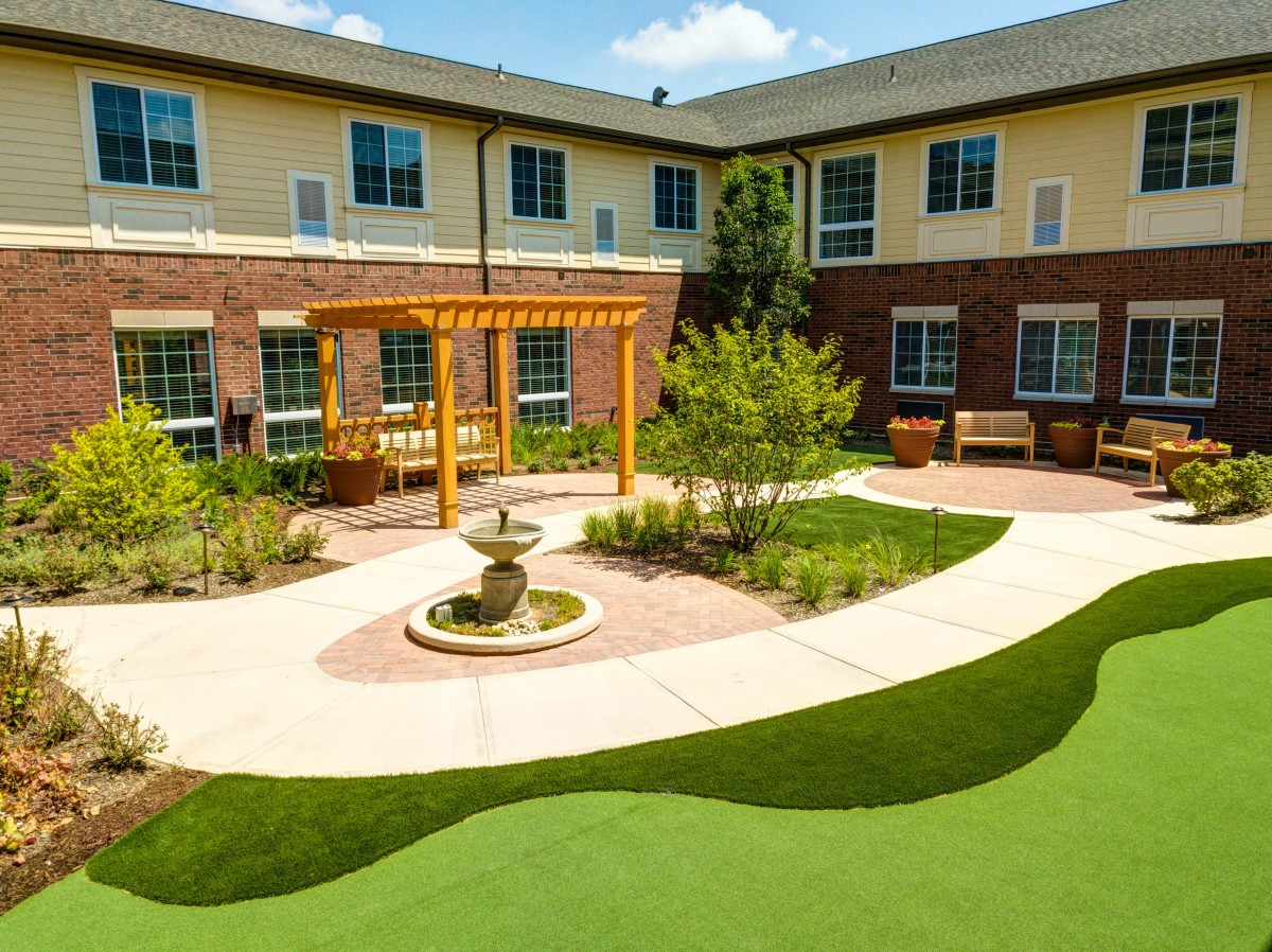 A serene courtyard with a fountain, surrounded by a well-maintained garden and comfortable seating.