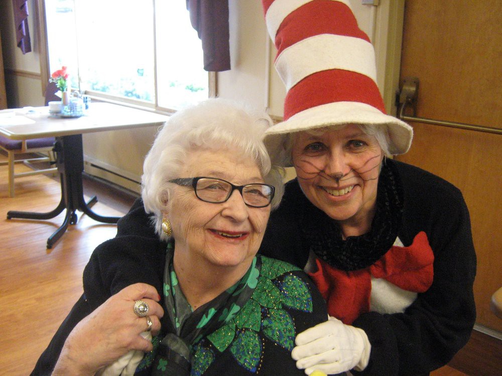 Two women smiling, one wearing a tall, striped hat and costume.