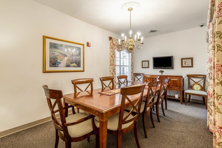 Elegant dining room with a long wooden table and chairs, adorned by a chandelier and wall decor.
