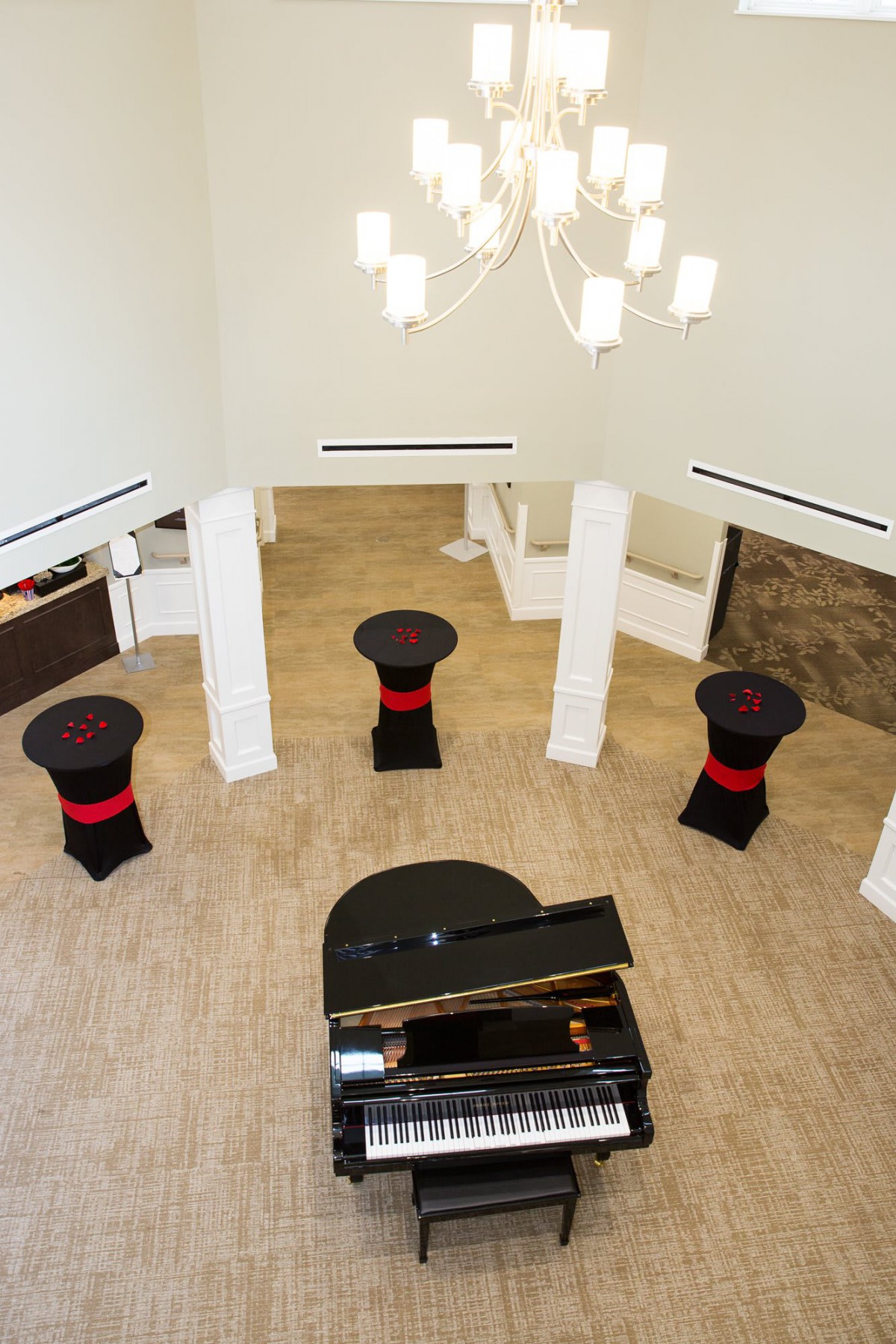 An elegant indoor space with a piano and round tables set up, featuring a modern chandelier.