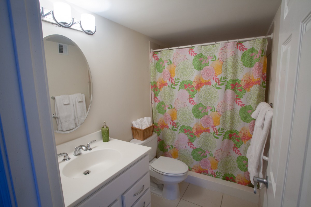 A neatly arranged bathroom featuring a sink with a mirror, a colorful shower curtain, and basic amenities.