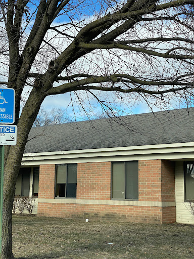 A building with a handicap parking sign in front, accompanied by a bare tree against a cloudy sky.