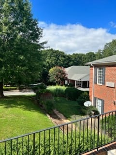 A view of a red brick apartment building surrounded by lush greenery and a well-maintained lawn.