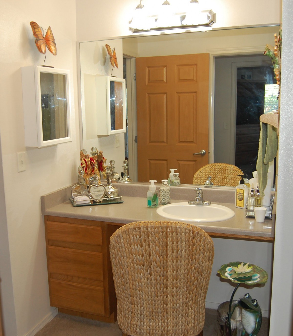 A neatly organized bathroom vanity with a large mirror, wicker chair, and various toiletries.