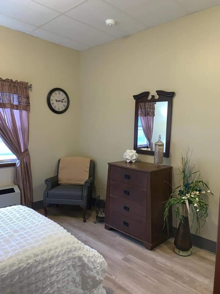 A cozy bedroom with a chair, dresser, and wall-mounted mirror.