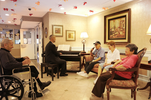 A performer plays the piano for a group of elderly residents in a cozy common area, fostering community and enjoyment through music.