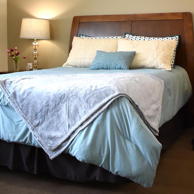 A neatly made bed with blue and white bedding, complemented by pillows and a bedside lamp.