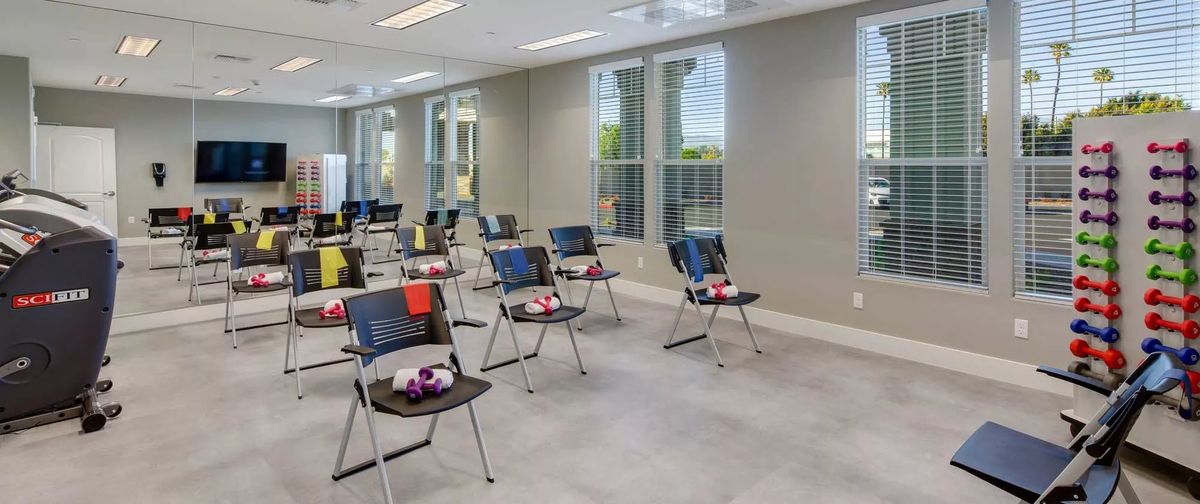 An organized classroom with chairs and small tables arranged in rows, and large windows allowing natural light to enter.