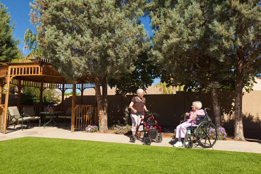 Two elderly individuals enjoying time outdoors in a garden setting, one using a wheelchair and the other assisting.