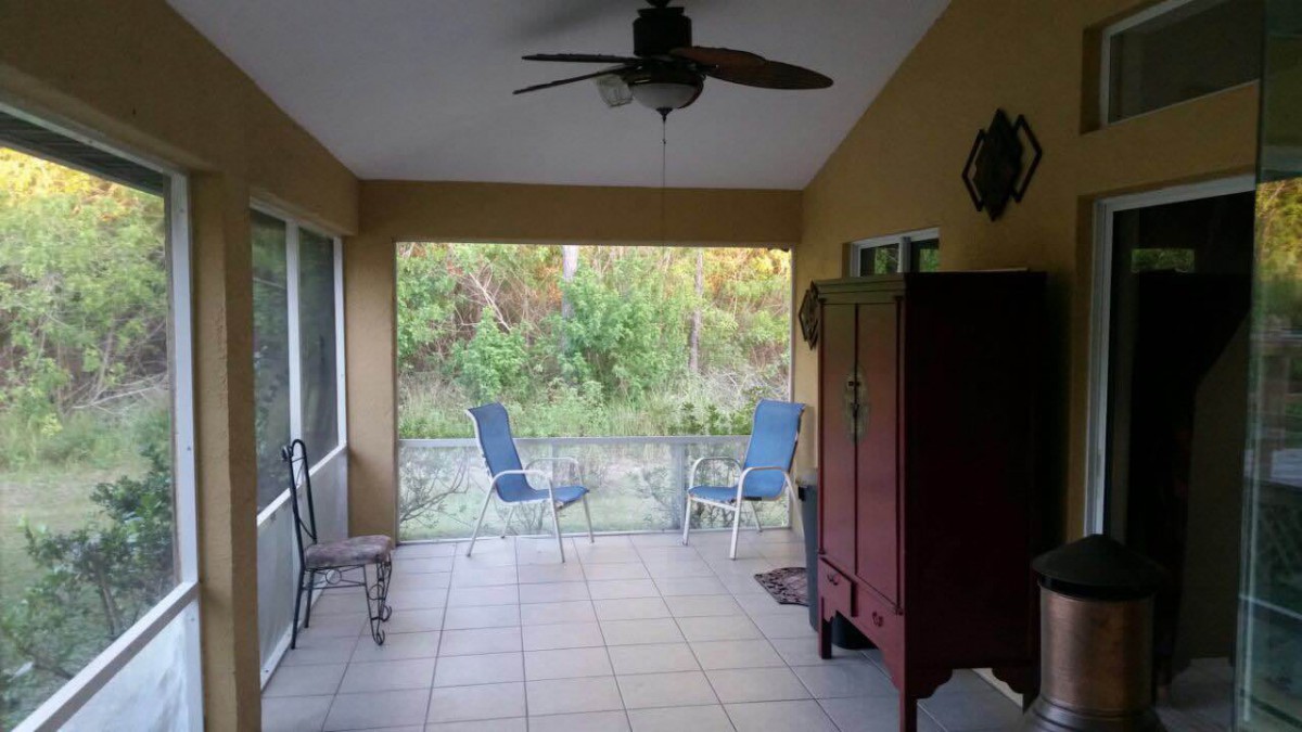 A cozy screened patio with chairs and a ceiling fan overlooking nature.