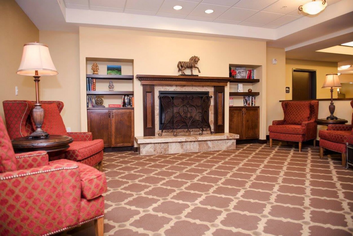 A cozy living room with a fireplace, featuring red armchairs and a patterned carpet.