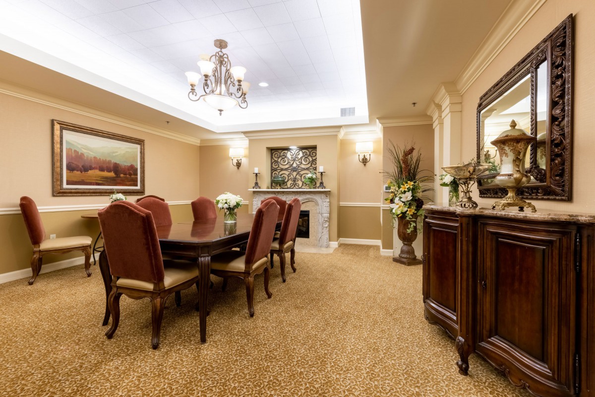 An elegantly decorated dining room featuring a chandelier, long dining table, cushioned chairs, and a warm fireplace.