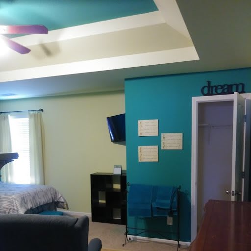 A cozy bedroom with colorful walls, featuring a ceiling fan and wall-mounted TV.