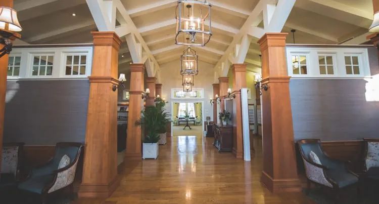 A spacious corridor featuring wooden pillars, elegant lighting fixtures, and decorative plants.