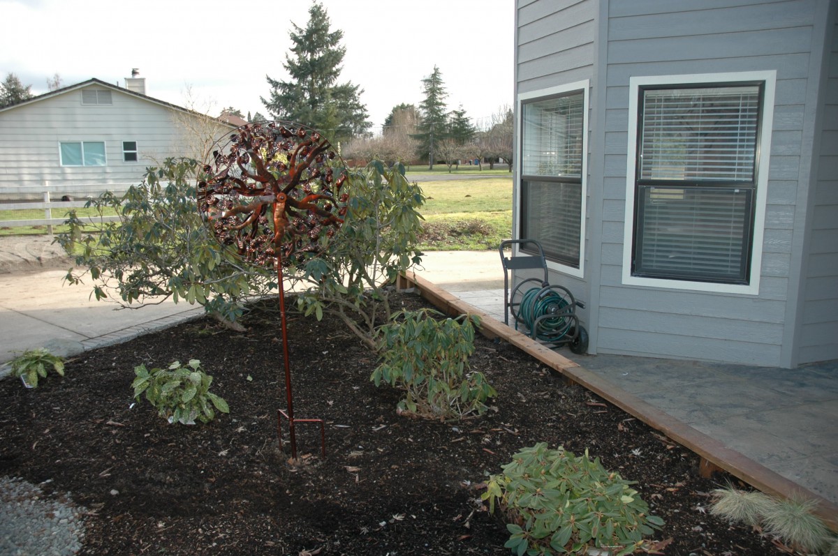 A garden featuring a metal sculpture next to a house.