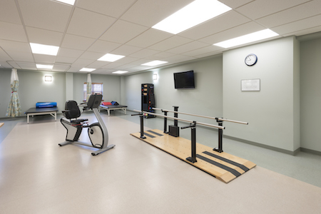 A physical therapy room equipped with a recumbent bike and parallel bars for rehabilitation exercises.