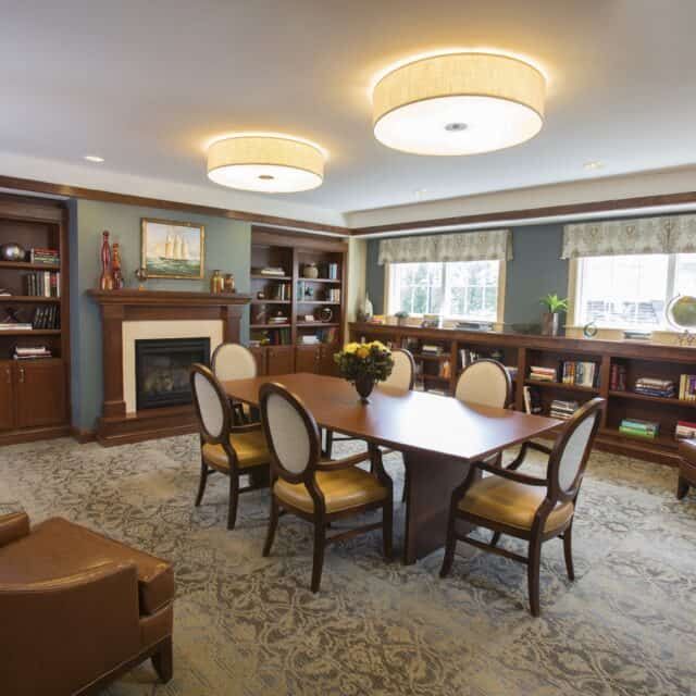 A cozy and elegant living room with a large dining table surrounded by chairs, bookshelves lining the walls, and a fireplace for added warmth.