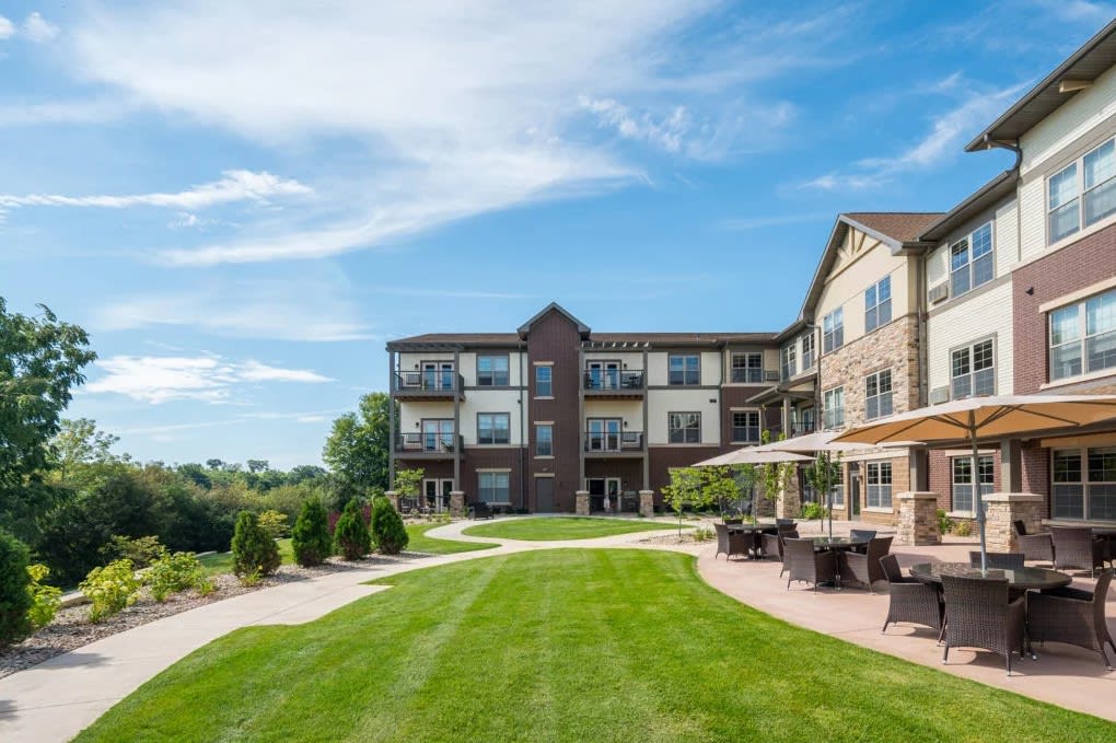 A modern apartment building with a well-maintained lawn and outdoor seating area under a bright blue sky.