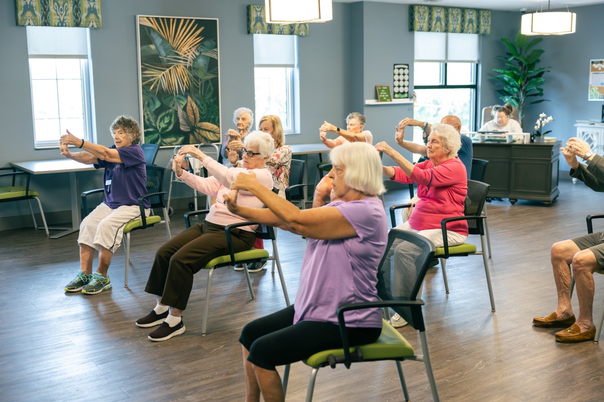 A group of elderly individuals participating in a chair exercise class indoors.