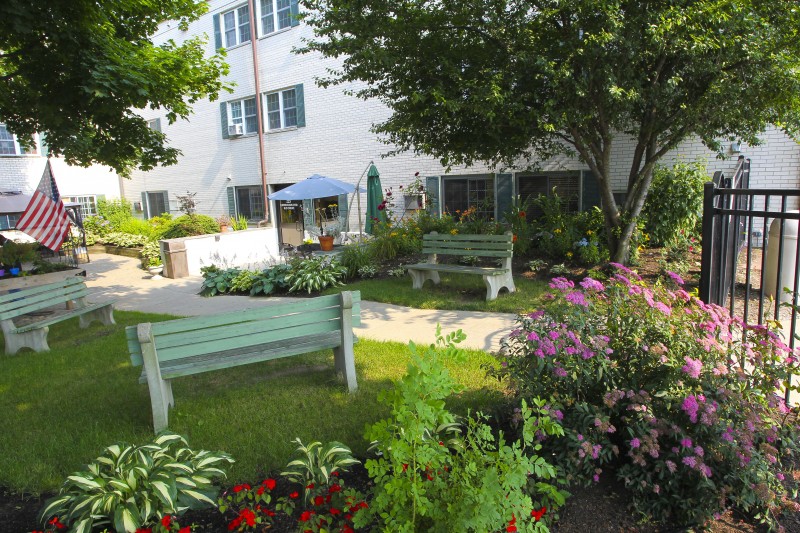 A peaceful garden area with benches, colorful flower beds, and a nearby building.