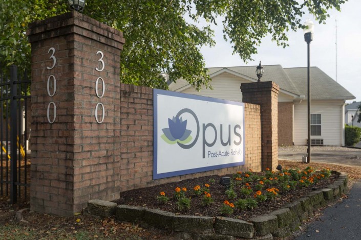 A business sign for Opus displayed on a brick wall near the entrance of a building, surrounded by landscaping.