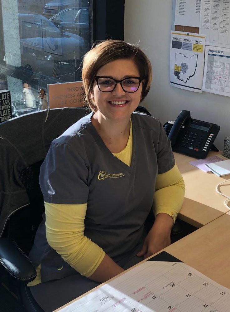 A woman wearing glasses is smiling while sitting at her office desk.