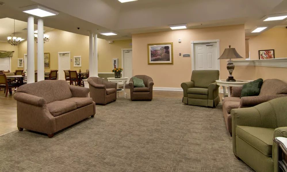 A spacious living room area featuring comfortable sofas and armchairs, adorned with a painting on the wall and a carpeted floor.